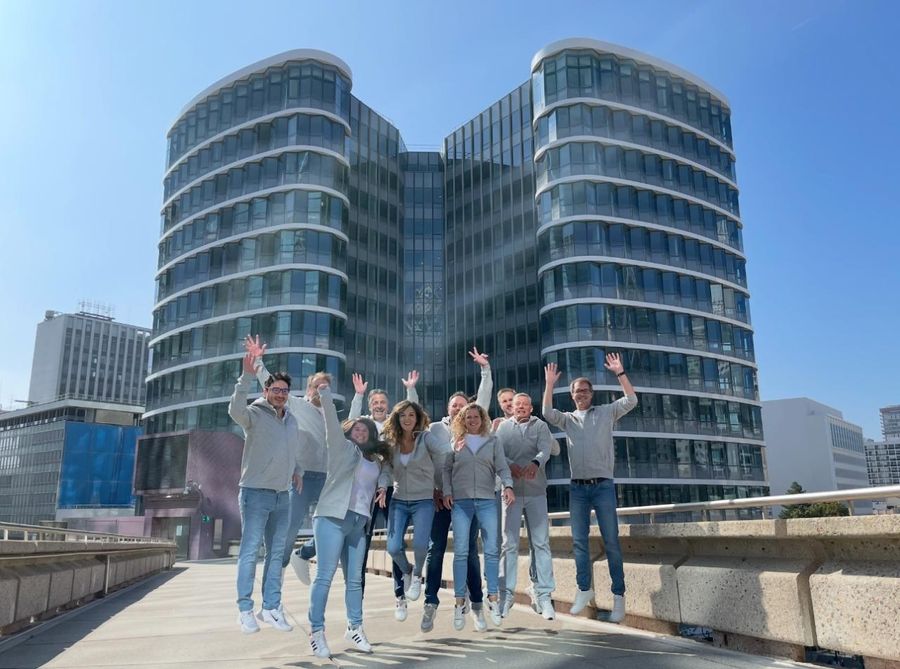 Une équipe d’une dizaine de personnes sautant en l’air, bras levés, devant le bâtiment du Campus Cyber à La Défense.