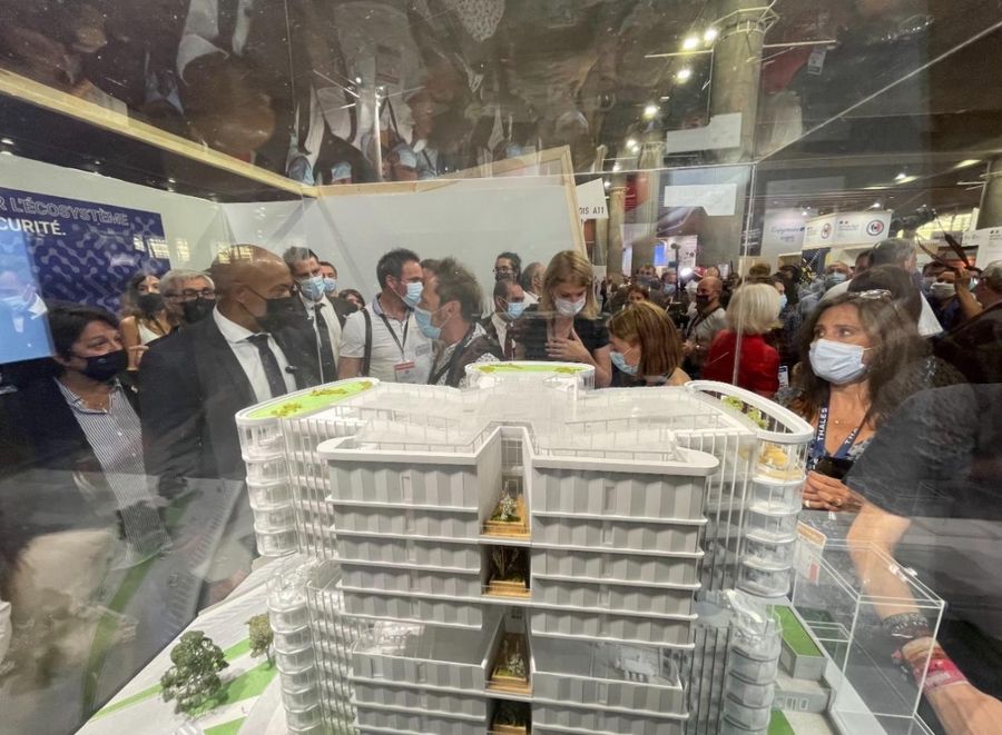 Foule masquée regardant à travers une vitrine la maquette architecturale du futur Campus Cyber, lors du Forum International de la Cybersécurité.